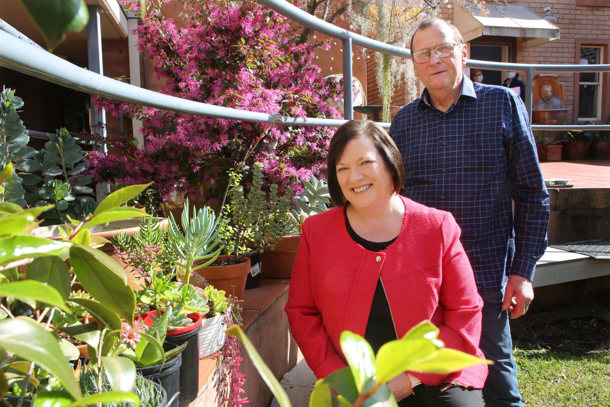 Karen and Geoff Diefenbach sit in the garden of Bezzina House, surrounded by lush plants